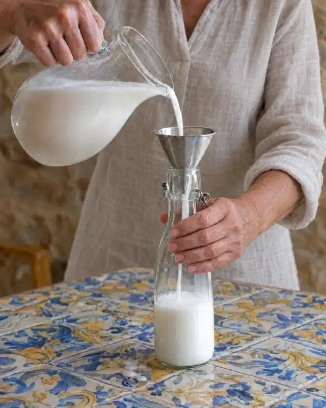Versare il latte di mandorla attraverso un imbuto in una bottiglia di vetro