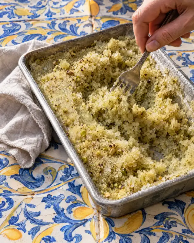 Granita al pistacchio lavorata con una forchetta in una teglia di metallo